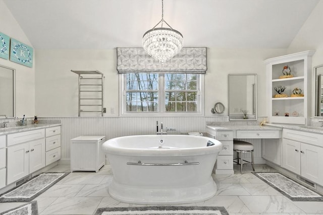 full bathroom featuring marble finish floor, a freestanding tub, vanity, vaulted ceiling, and wainscoting