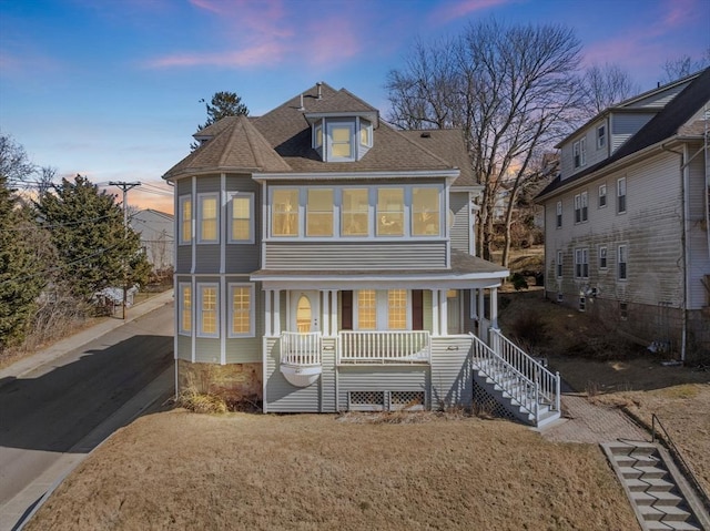 back of house at dusk featuring stairway, covered porch, and a shingled roof