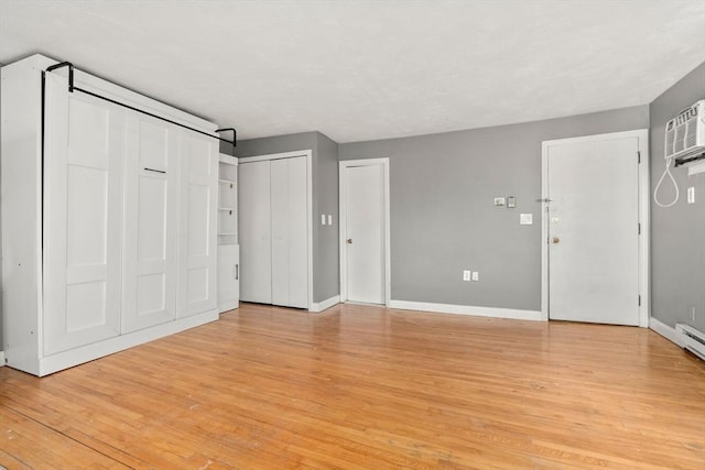 unfurnished bedroom with a wall mounted AC, two closets, light wood-type flooring, and baseboards