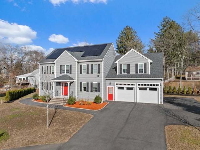 view of front of house featuring roof mounted solar panels, a garage, driveway, and roof with shingles