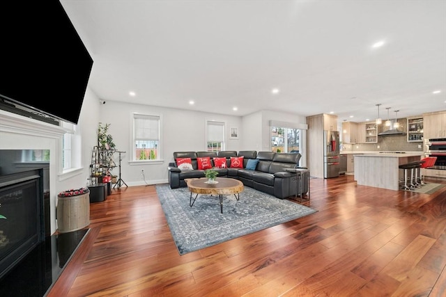 living area with recessed lighting, plenty of natural light, dark wood-type flooring, and a glass covered fireplace