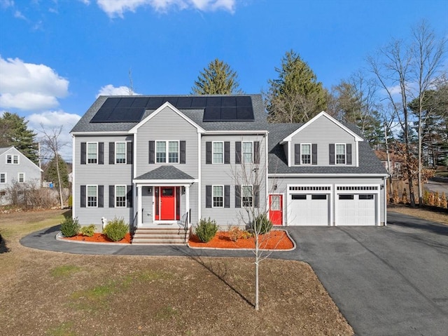 colonial-style house with solar panels, driveway, a garage, and roof with shingles