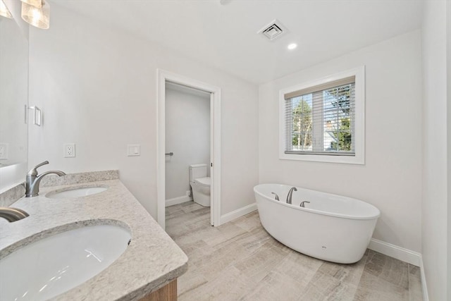 bathroom featuring double vanity, toilet, a freestanding bath, and a sink