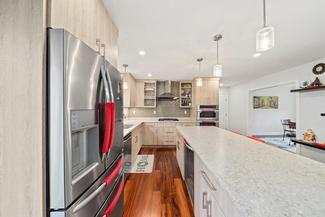 kitchen with light brown cabinetry, tasteful backsplash, stainless steel appliances, wall chimney exhaust hood, and dark wood-style flooring