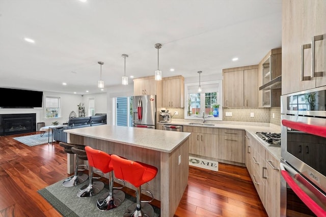 kitchen with light brown cabinets, a kitchen island, dark wood-style flooring, a sink, and appliances with stainless steel finishes