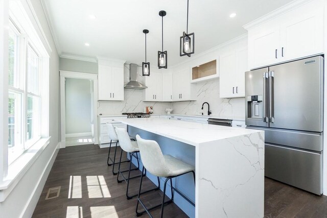 kitchen featuring wall chimney exhaust hood, a center island, stainless steel appliances, white cabinetry, and decorative backsplash
