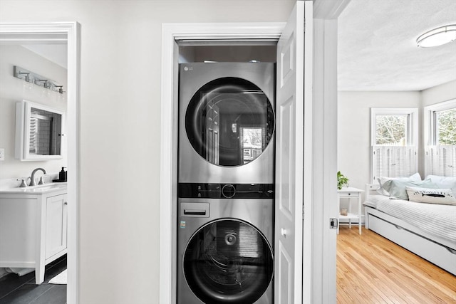 laundry area with stacked washing maching and dryer, sink, and wood-type flooring