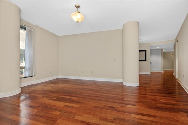 unfurnished room with decorative columns, baseboards, and wood finished floors