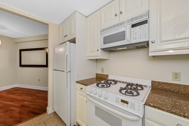 kitchen featuring white appliances, dark stone countertops, light tile patterned floors, baseboards, and white cabinetry