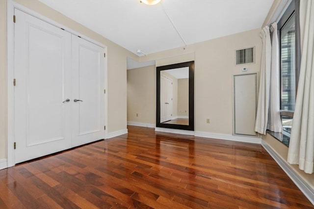 unfurnished bedroom featuring wood finished floors, visible vents, a closet, and baseboards