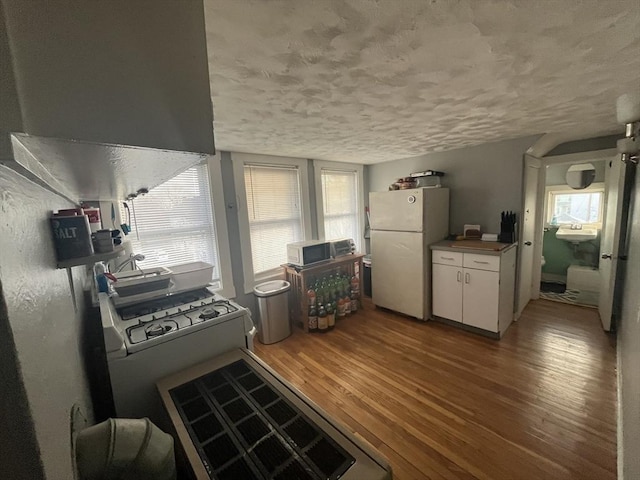 kitchen with white cabinets, ventilation hood, light wood-type flooring, and white fridge