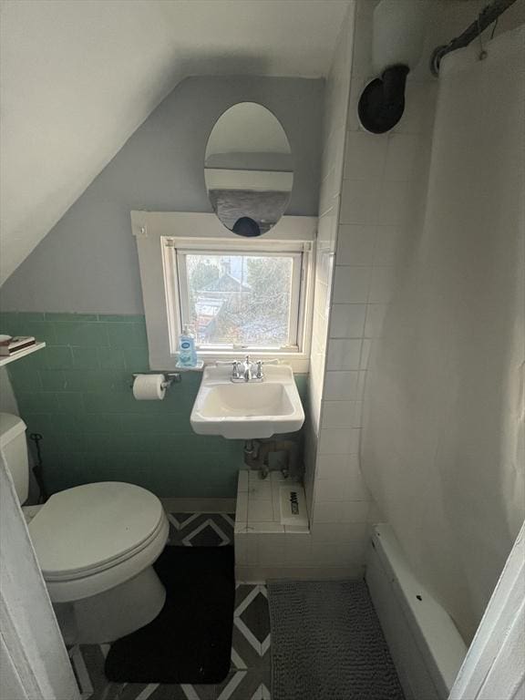 bathroom featuring vaulted ceiling, toilet, tile walls, and sink