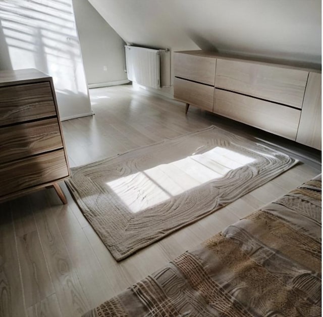 unfurnished bedroom featuring lofted ceiling, wood-type flooring, and radiator