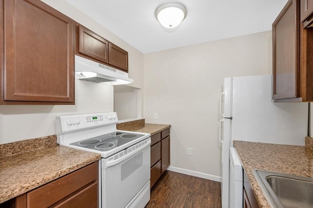 kitchen with under cabinet range hood, white appliances, baseboards, brown cabinets, and dark wood-style floors