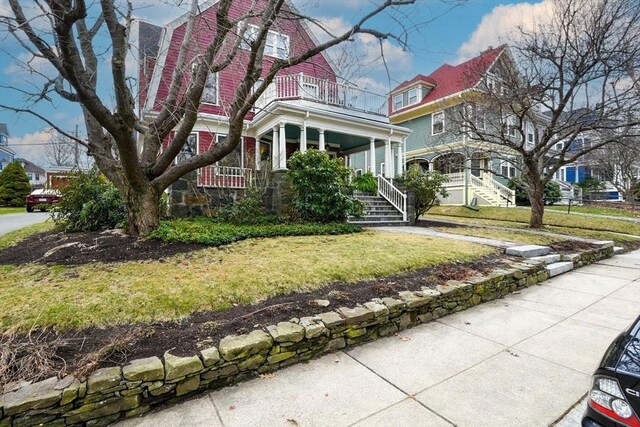 victorian-style house with a balcony, a gambrel roof, a front yard, and covered porch