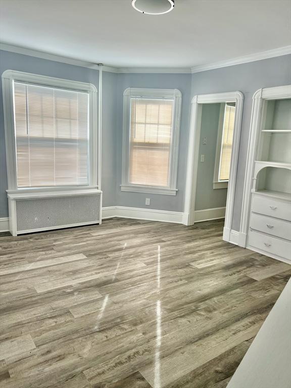 unfurnished bedroom with radiator, crown molding, baseboards, and wood finished floors