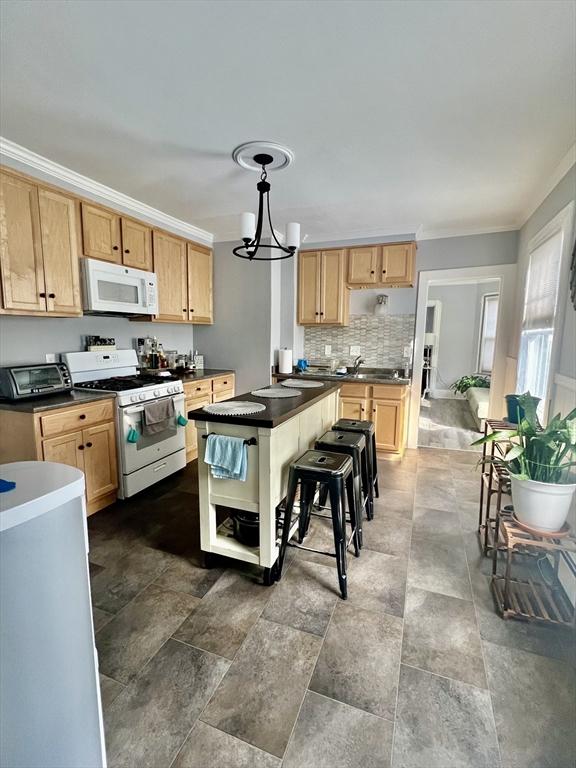 kitchen featuring white appliances, dark countertops, light brown cabinets, and crown molding