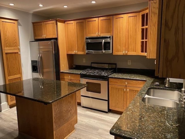 kitchen featuring dark stone countertops, stainless steel appliances, light wood-type flooring, and a sink