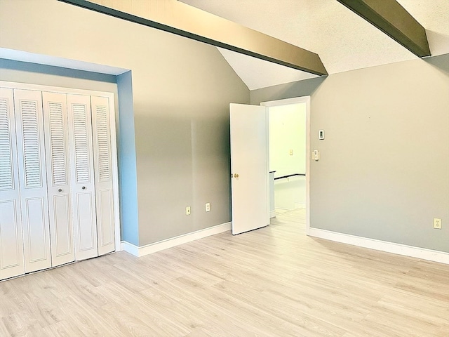 unfurnished bedroom with a textured ceiling, lofted ceiling with beams, light hardwood / wood-style flooring, and a closet