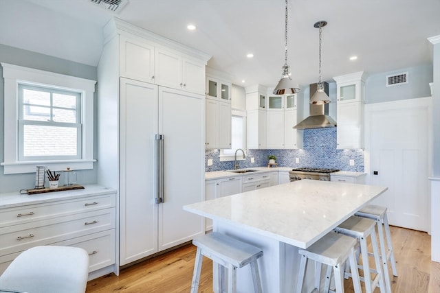 kitchen with light hardwood / wood-style floors, wall chimney exhaust hood, a center island, and white cabinets