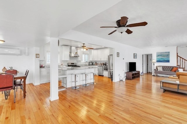 living room with an AC wall unit, sink, light wood-type flooring, and ceiling fan