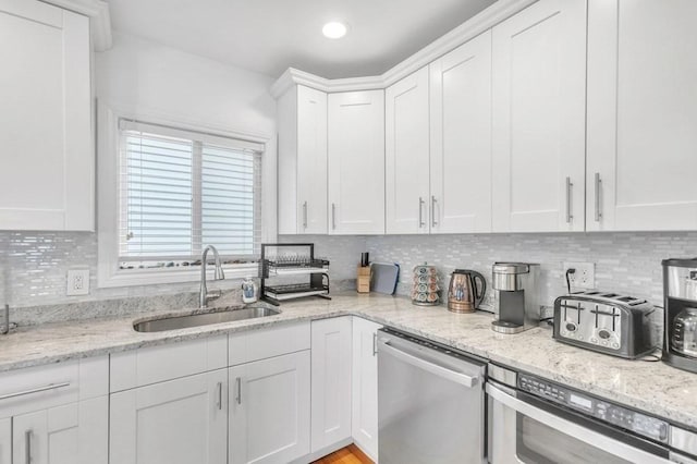 kitchen with light stone countertops, white cabinets, stainless steel dishwasher, decorative backsplash, and sink