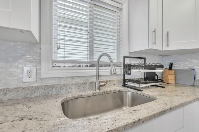 kitchen with sink, backsplash, white cabinets, and light stone counters