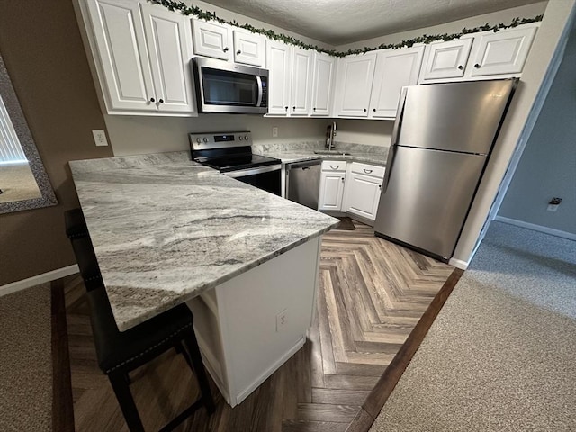 kitchen with baseboards, a kitchen breakfast bar, a peninsula, stainless steel appliances, and white cabinetry
