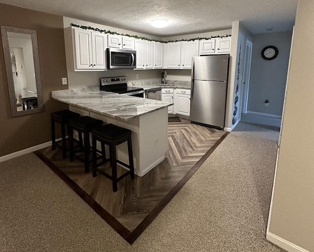 kitchen with baseboards, a peninsula, stainless steel appliances, a textured ceiling, and white cabinetry