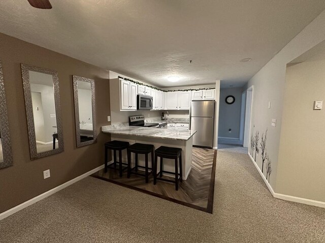 kitchen with appliances with stainless steel finishes, a peninsula, white cabinets, light countertops, and baseboards