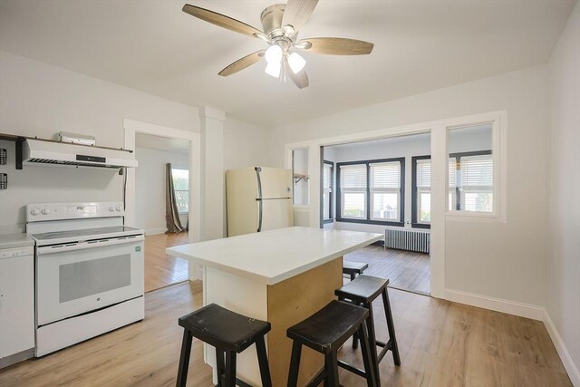 kitchen with radiator, white appliances, baseboards, a kitchen breakfast bar, and exhaust hood