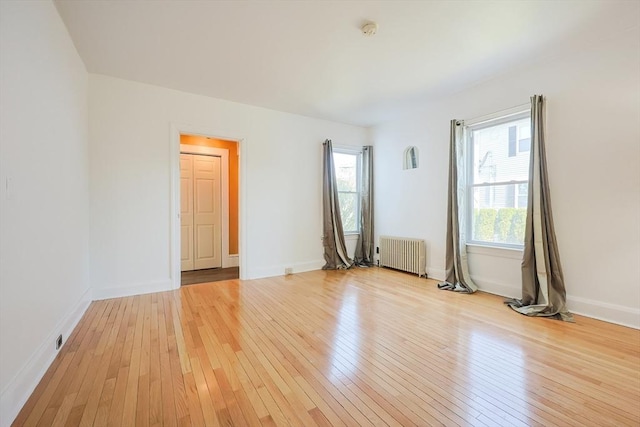 unfurnished room with radiator heating unit, baseboards, and light wood-style floors