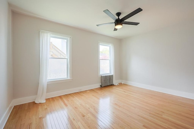 empty room featuring radiator heating unit, baseboards, a ceiling fan, and hardwood / wood-style flooring