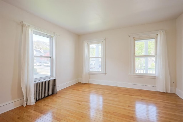 unfurnished room with baseboards, radiator, and light wood finished floors