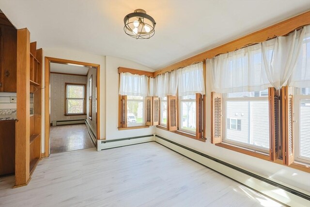 empty room featuring light wood-style flooring, lofted ceiling, and a baseboard radiator