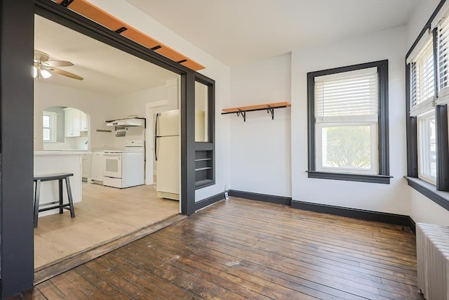 interior space with arched walkways, a ceiling fan, radiator heating unit, and light wood-style flooring