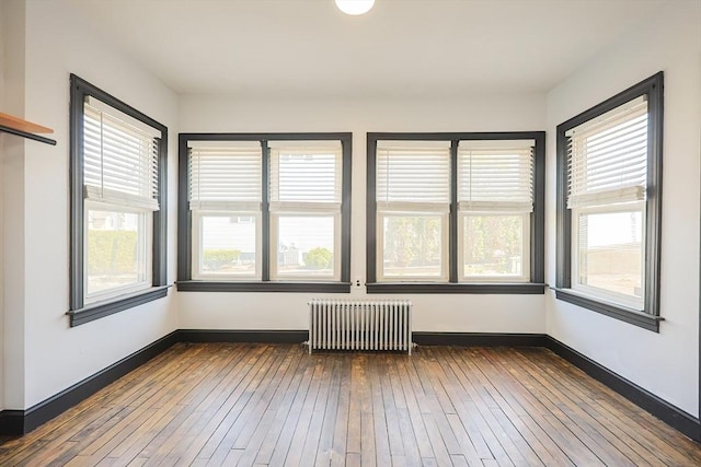 unfurnished sunroom with baseboards, plenty of natural light, radiator heating unit, and hardwood / wood-style flooring