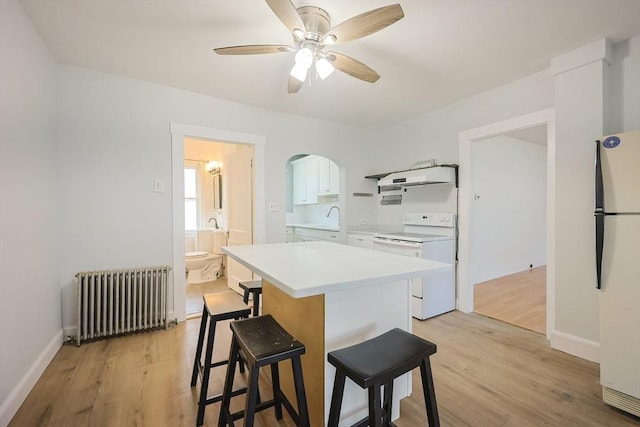 kitchen featuring light wood-style floors, white appliances, a breakfast bar area, light countertops, and radiator