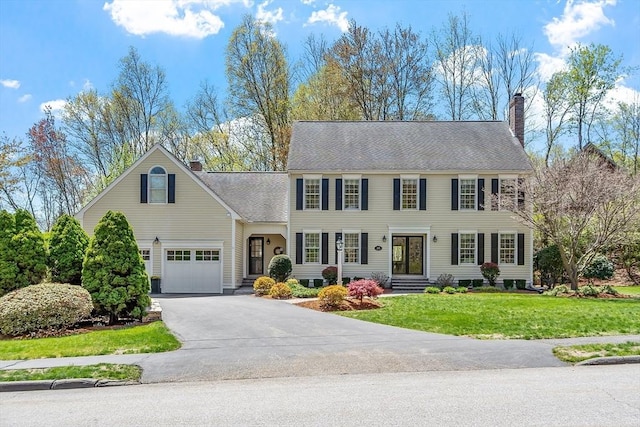 colonial-style house with entry steps, a chimney, a front yard, and aphalt driveway