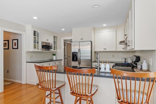 kitchen featuring a peninsula, glass insert cabinets, white cabinetry, backsplash, and stainless steel appliances