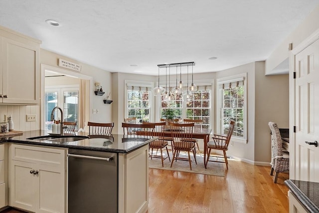 kitchen featuring pendant lighting, a peninsula, light wood-style floors, a sink, and dishwasher