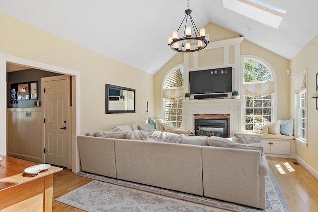 living room with a brick fireplace, high vaulted ceiling, a notable chandelier, and light wood-style floors