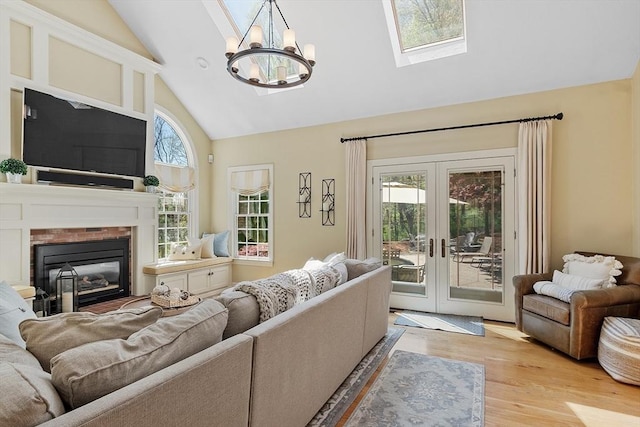 living room with an inviting chandelier, a fireplace, high vaulted ceiling, light wood-type flooring, and french doors