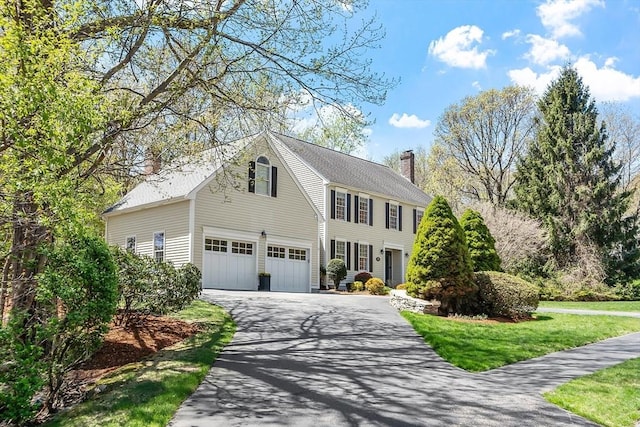 colonial house with a garage, a chimney, driveway, and a front yard