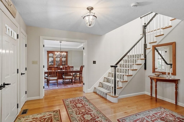 foyer with visible vents, light wood-type flooring, stairway, baseboards, and a chandelier