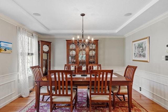 dining space featuring a raised ceiling, light wood finished floors, and a notable chandelier