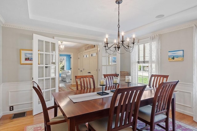 dining area featuring a notable chandelier, a decorative wall, a wainscoted wall, light wood-type flooring, and visible vents
