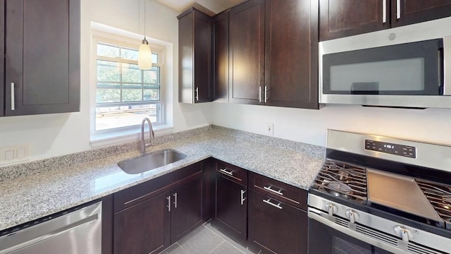 kitchen with dark brown cabinets, light stone countertops, pendant lighting, stainless steel appliances, and a sink