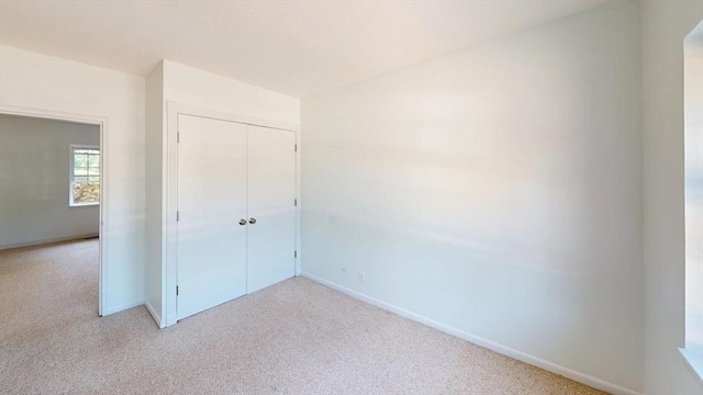 unfurnished bedroom featuring light colored carpet, a closet, and baseboards