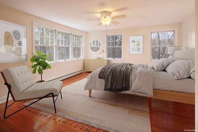 bedroom featuring baseboard heating, multiple windows, a ceiling fan, and wood-type flooring